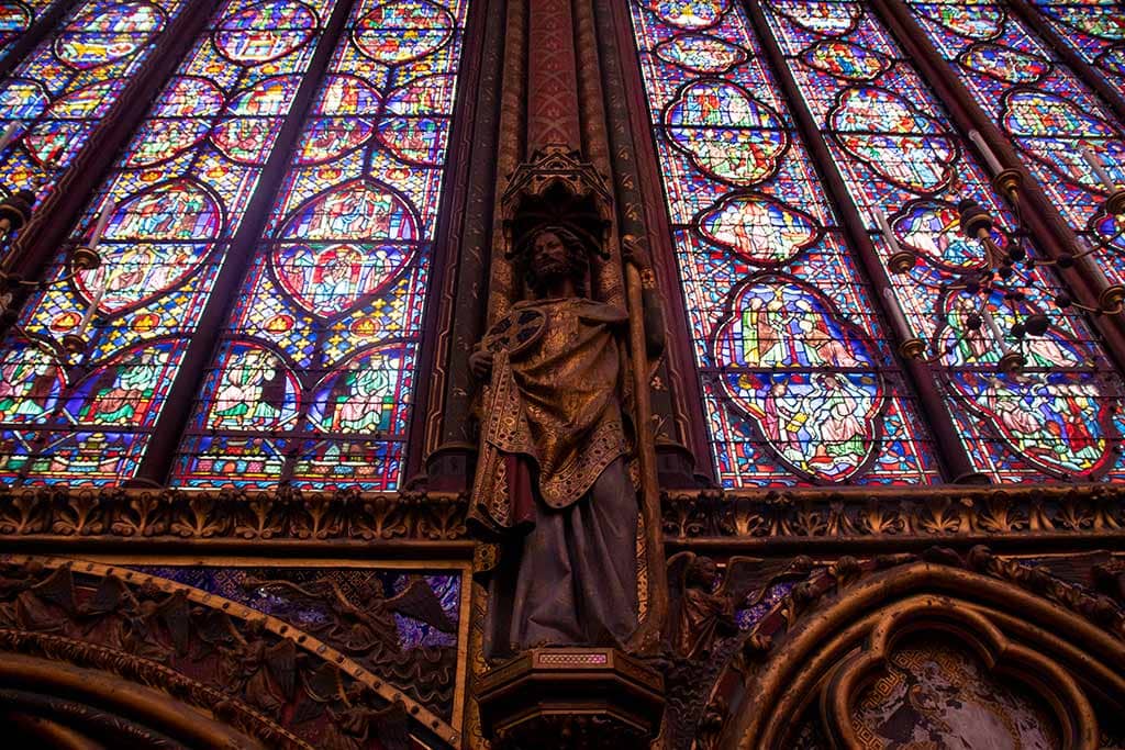 Visiting La Sainte Chapelle Paris: A complete guide Image of a statue of an apostle and stained glass windows in La Sainte Chapelle Paris